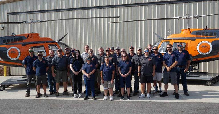 Team of 27 people standing in front of 2 helicopters.
