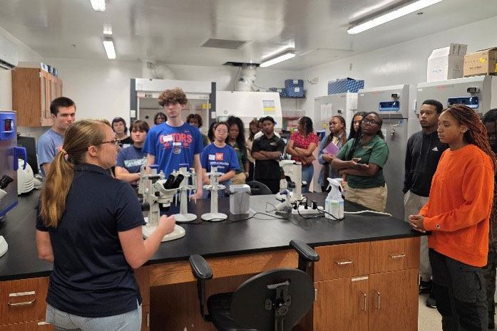 A mosquito control professional talks to a group of students during a visit to a science lab.
